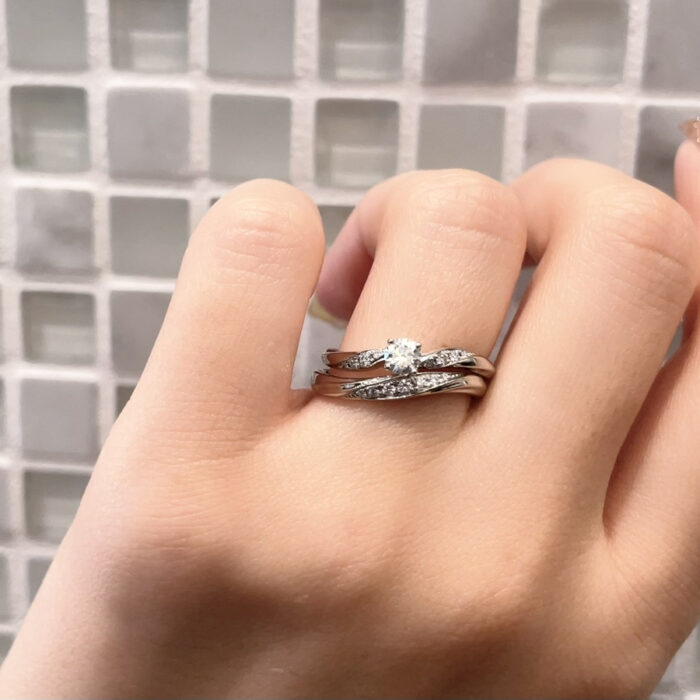 ウェーブの結婚指輪と婚約指輪を重ねづけしている手元